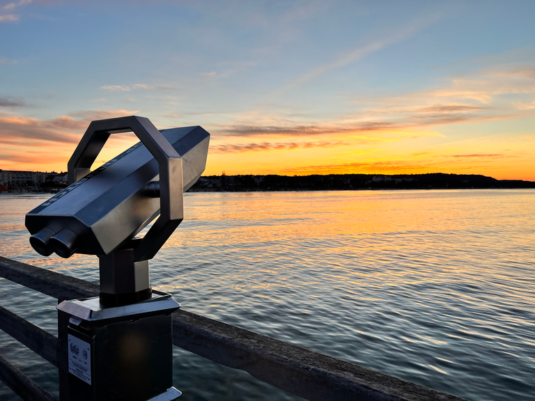Ein Münzfernglas im Sonnenuntergang auf der Seebrücke in Binz, der Sonnenuntergang spiegelt sich in der Ostsee.